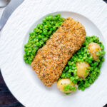 Overhead baked cod loin in crispy panko breadcrumbs with crushed minted peas and potatoes featuring a title overlay.