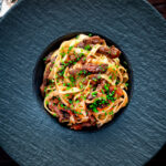 Overhead beef cheek ragu served with pappardelle pasta and snipped chives.