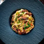 Overhead beef cheek ragu served with pappardelle pasta and snipped chives.