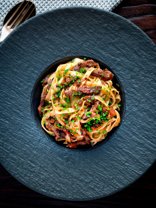 Overhead beef cheek ragu served with pappardelle pasta and snipped chives.