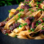 Close up beef cheek ragu served with pappardelle pasta and snipped chives.