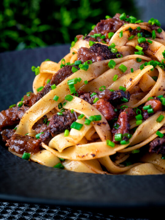 Close up beef cheek ragu served with pappardelle pasta and snipped chives.