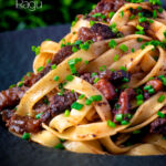 Close up beef cheek ragu served with pappardelle pasta and snipped chives featuring a title overlay.