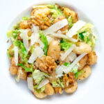 Overhead cabbage and walnut gnocchi served with parmesan shavings featuring a title overlay.