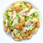 Overhead cabbage and walnut gnocchi served with parmesan shavings featuring a title overlay.