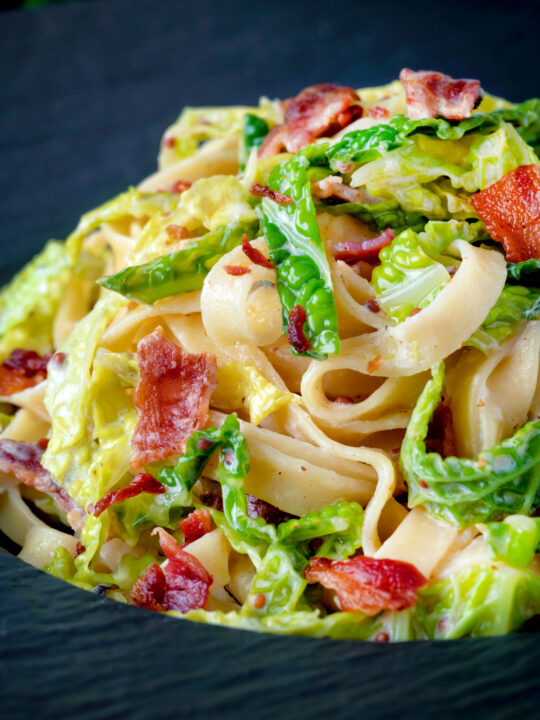 Close up creamy savoy cabbage pasta with crispy bacon and sour cream.