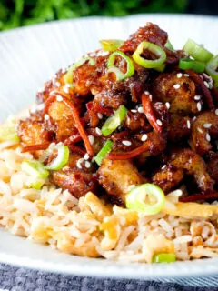 Close up Chinese takeaway style crispy orange chicken with egg fried rice.