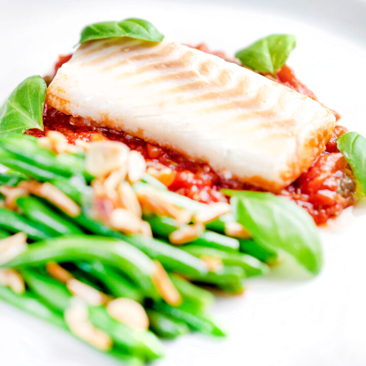 Baked cod loin in tomato sauce served with green beans amandine.
