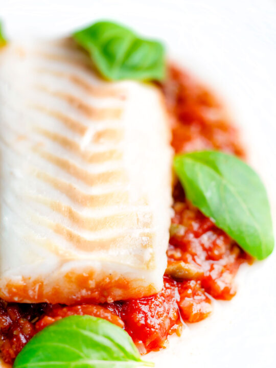 Close up baked cod loin in tomato sauce served with green beans.