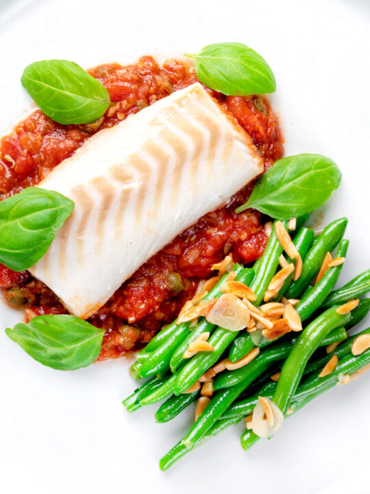 Overhead baked cod loin in tomato sauce served with green beans.