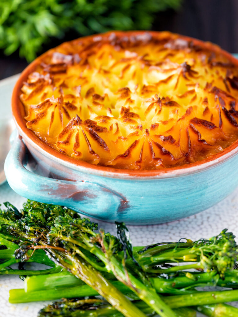 Individual traditional British mince beef cottage pie served in a blue earthenware bowl.
