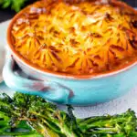 Individual traditional British mince beef cottage pie served in a blue earthenware bowl featuring a title overlay.