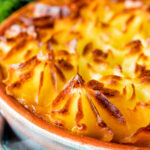 Close up traditional British mince beef cottage pie served in a blue earthenware bowl.