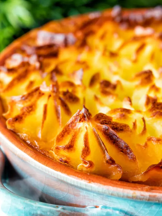 Close up traditional British mince beef cottage pie served in a blue earthenware bowl.