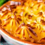 Close up traditional British mince beef cottage pie served in a blue earthenware bowl featuring a title overlay.