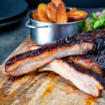 Oven baked sticky BBQ pork ribs served with salad and wedges.