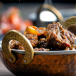 Steaming hot Anglo Goan pork vindaloo curry served in a kadai featuring a title overlay.