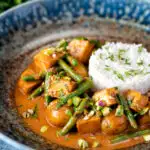 Vegan Thai massaman curry with potatoes, green beans and pistachio nuts featuring a title overlay.