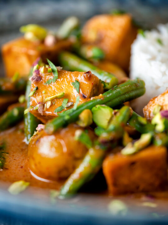 Close up vegan Thai massaman curry with potatoes, green beans and pistachio nuts.