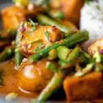 Close up vegan Thai massaman curry with potatoes, green beans and pistachio nuts featuring a title overlay.