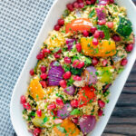 Overhead vegetarian roasted vegetable couscous salad with pomegranate arils featuring a title overlay.