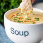 Bread being dipped into a cream of celeriac soup served in a cup.