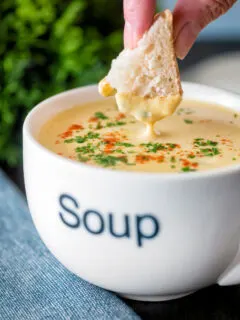 Bread being dipped into a cream of celeriac soup served in a cup.