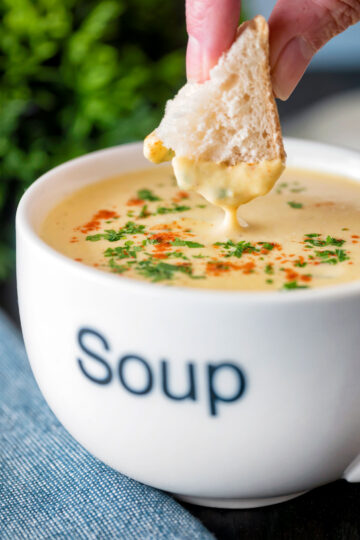Bread being dipped into a cream of celeriac soup served in a cup.