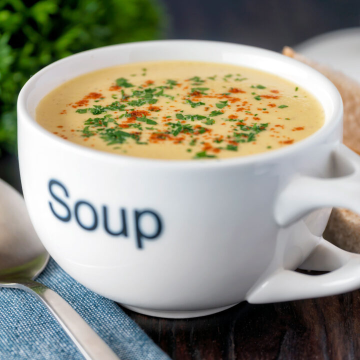 Creamy celeriac soup served in a cup garnished with parsley and paprika.