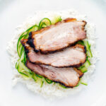 Overhead sliced crispy Chinese Pork Belly served with rice and pickled cucumbers.