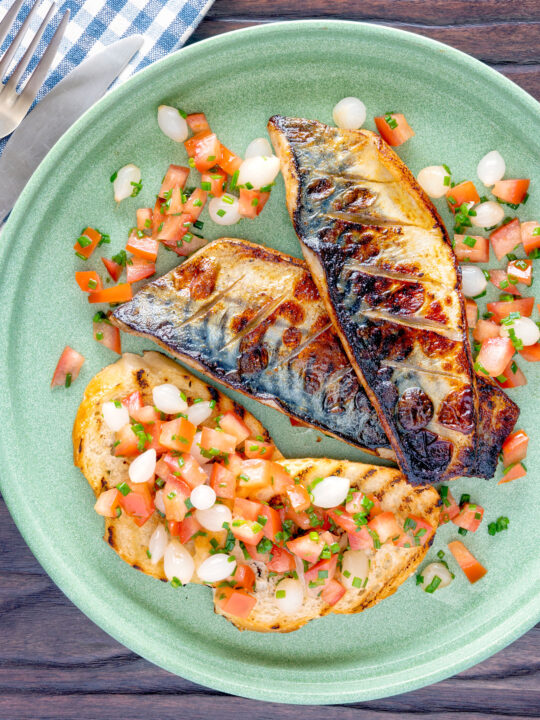 Overhead devilled mackerel fillets served with a pickled onion and tomato salad.