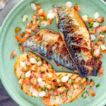 Overhead devilled mackerel fillets served with a pickled onion and tomato salad featuring a title overlay.