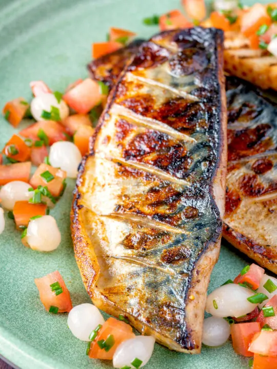Close up devilled mackerel fillets served with a pickled onion and tomato salad.