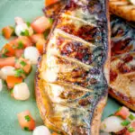Close up devilled mackerel fillets served with a pickled onion and tomato salad featuring a title overlay.