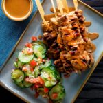 Overhead pork satay skewers with peanut dipping sauce featuring a title overlay.