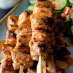 Close up pork satay skewers with peanut dipping sauce.
