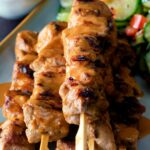 Close up pork satay skewers with peanut dipping sauce featuring a title overlay.