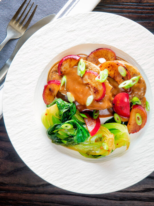 Overhead pork tenderloin with plum sauce, fresh plums and pak choi.