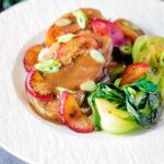 Pork tenderloin with plum sauce, fresh plums and pak choi.