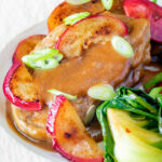 Close up pork tenderloin with plum sauce, fresh plums and pak choi.
