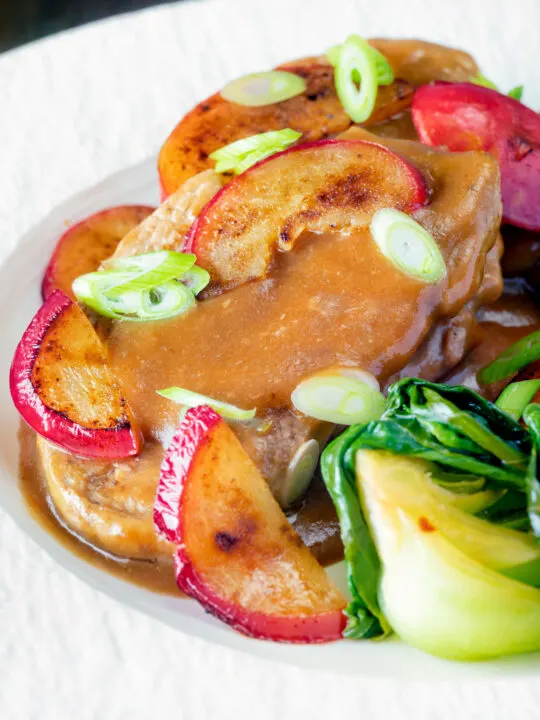 Close up pork tenderloin with plum sauce, fresh plums and pak choi.