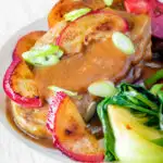 Close up pork tenderloin with plum sauce, fresh plums and pak choi featuring a title overlay.