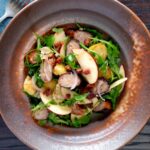 Overhead sausage salad with apple, new potatoes, bacon and rocket or arugula.