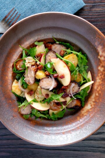 Overhead sausage salad with apple, new potatoes, bacon and rocket or arugula.