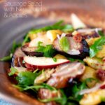 Sausage salad with apple, new potatoes, bacon and rocket or arugula featuring a title overlay.