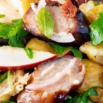 Close up sausage salad with apple, new potatoes, bacon and rocket or arugula.