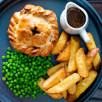 Overhead hand raised steak and ale pie with chips and peas.