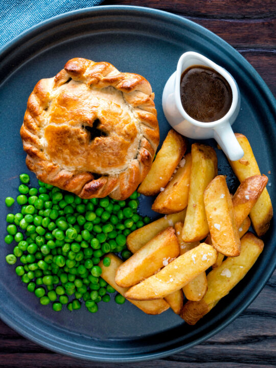Overhead hand raised steak and ale pie with chips and peas.