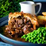Individual steak and ale pie cut open to show filling served with chips and peas.