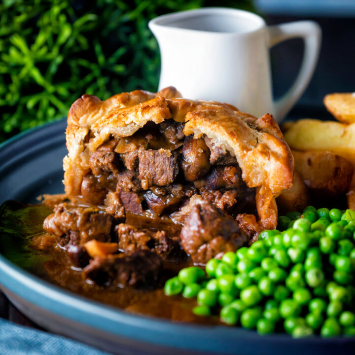 Individual steak and ale pie cut open to show filling served with chips and peas.